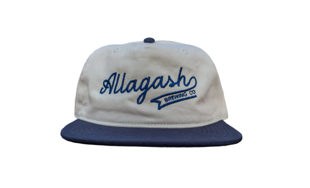 The front of a ballcap featuring the text "Allagash Brewing Co." in blue on a cream cap.
