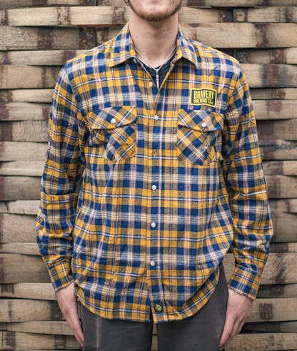 front of yellow and blue Flannel shirt worn by a model. Above the wearer's left chest pocket is an embroidered black and yellow patch with Bravery Brewing Co.'s logo.