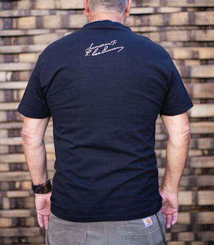 back of Gunny black t-shirt worn by a male model. The text "Semper Fi R. Lee Ermey" in a handwritten script is printed small below the back collar in light brown ink.