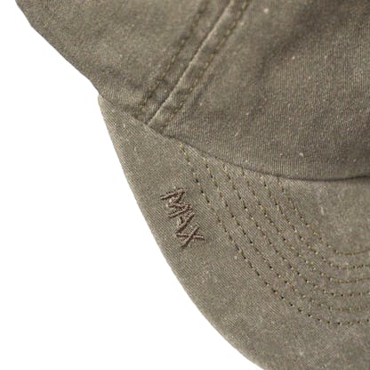Detail photo of green hat's bill on a white background. On the bill the text "max" is embroidered small in the same green color of the hat along the edge of the bill.