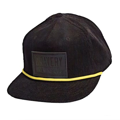 Front side photo of a black corduroy snapback on a white background. The hat has a thick yellow cord along where the brim meets the hat, and a black leather patch on the front two panels. The leather patch has the logo for Bravery etched on it.