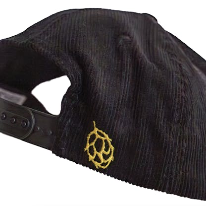 Side detail photo of a black corduroy snapback on a white background. There is an icon of a hop embroidered in yellow along the back right side of the hat.