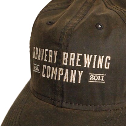 Front detail photo of brown baseball cap on a white background. The hat is a lightly worn weathered material with white embroidered text across the front two panels that says "BRAVERY BREWING COMPANY est 2011."