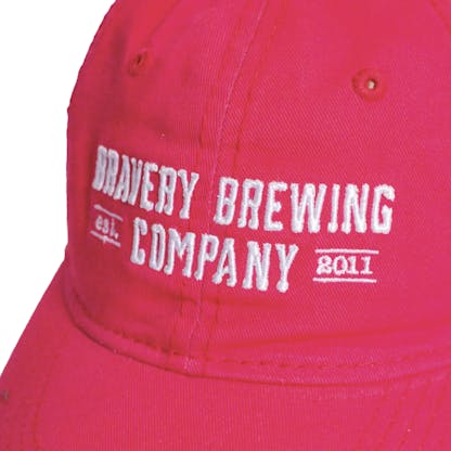 Front detail photo of bright pink baseball cap on a white background. The fabric hat has white embroidered text across the front two panels that says "BRAVERY BREWING COMPANY est 2011."