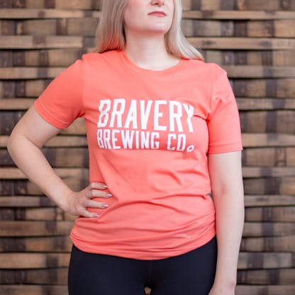 Photo of a person wearing a shirt facing the camera. The shirt is coral in color with the text "Bravery Brewing Co." printed in white large across the chest.