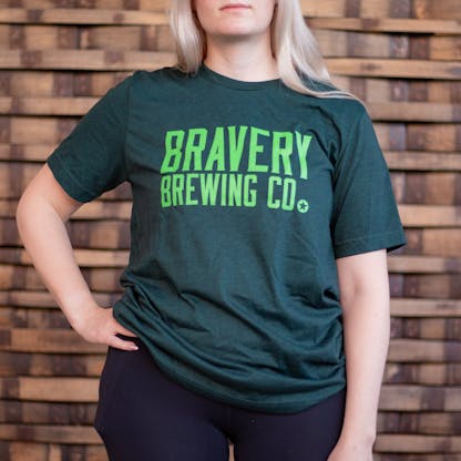 Photo of a person wearing a shirt facing the camera. The shirt is a dark heather green in color with the text "Bravery Brewing Co." printed in bright green large across the chest.