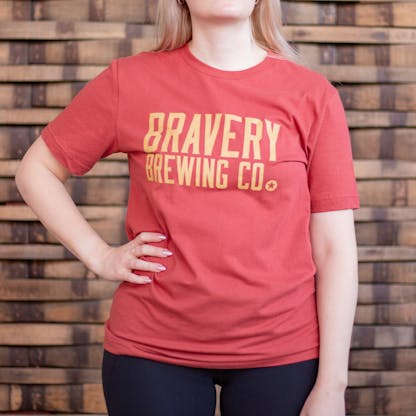 Photo of a person wearing a shirt facing the camera. The shirt is red in color with the text "Bravery Brewing Co." printed in gold large across the chest.