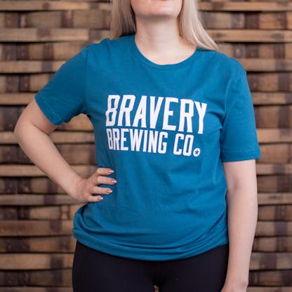 Photo of a person wearing a shirt facing the camera. The shirt is teal in color with the text "Bravery Brewing Co." printed in white large across the chest.