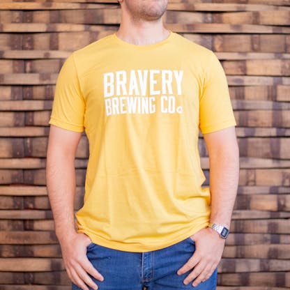 Photo of a person wearing a shirt facing the camera. The shirt is yellow in color with the text "Bravery Brewing Co." printed in white large across the chest.