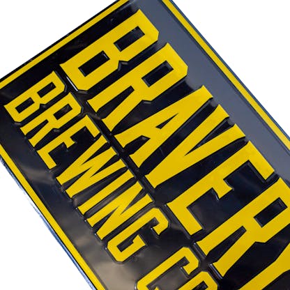 Detail photo of the tin tacker. The Metal sign is at an angle and has the text "Bravery Brewing Co." embossed in yellow on a black background.
