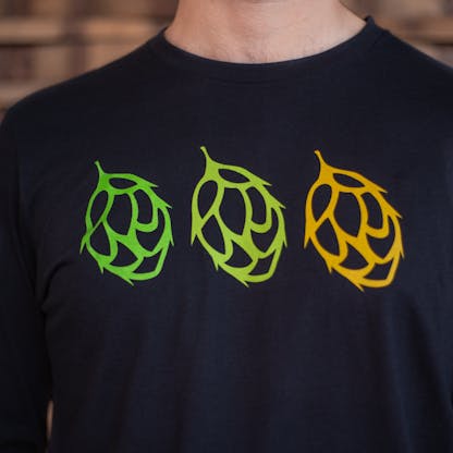 Detail photo of a person wearing a black long sleeve shirt from the front. The front of the shirt has the icons of three duplicate hops across the chest, from left to right they are vibrant green, light green, and yellow in color.