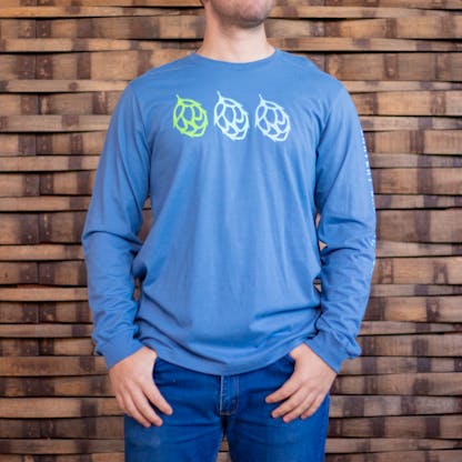 Photo of a person wearing a light blue long sleeve shirt from the front. The front of the shirt has the icons of three duplicate hops across the chest, from left to right they are green, white, and pale blue in color.