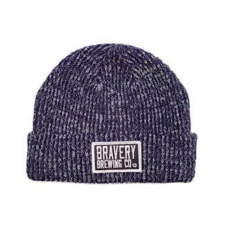 Photo of a knit beanie laying flat on a white background with a black and white embroidered patch sewn on the front. The hat is a blue and white marbled yarn and the patch has the text "Bravery Brewing Co." embroidered in white onto it.