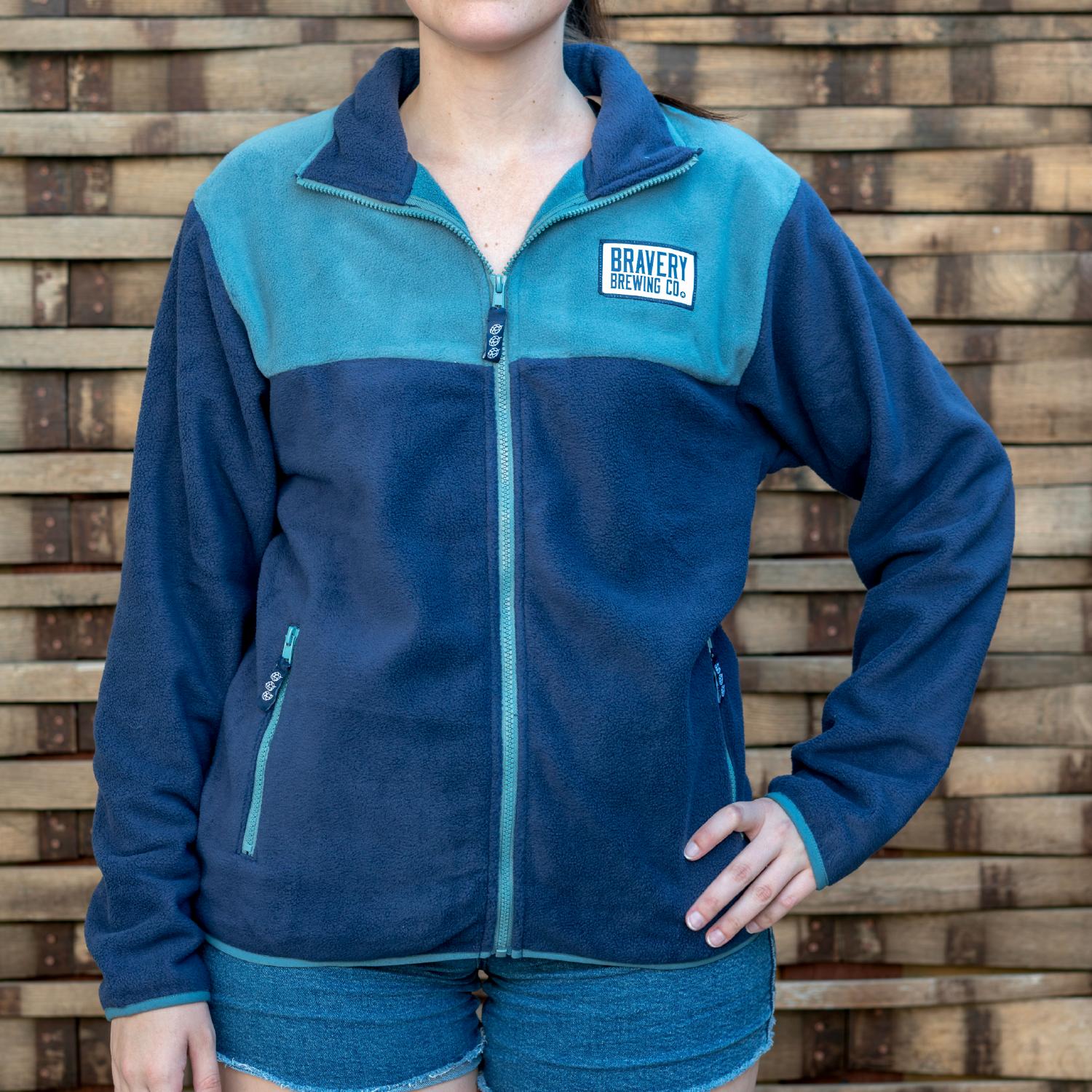 Front of blue fleece jacket worn by a model. Above the wearer's left chest pocket is a sewn on patch with Bravery Brewing Co.'s logo.