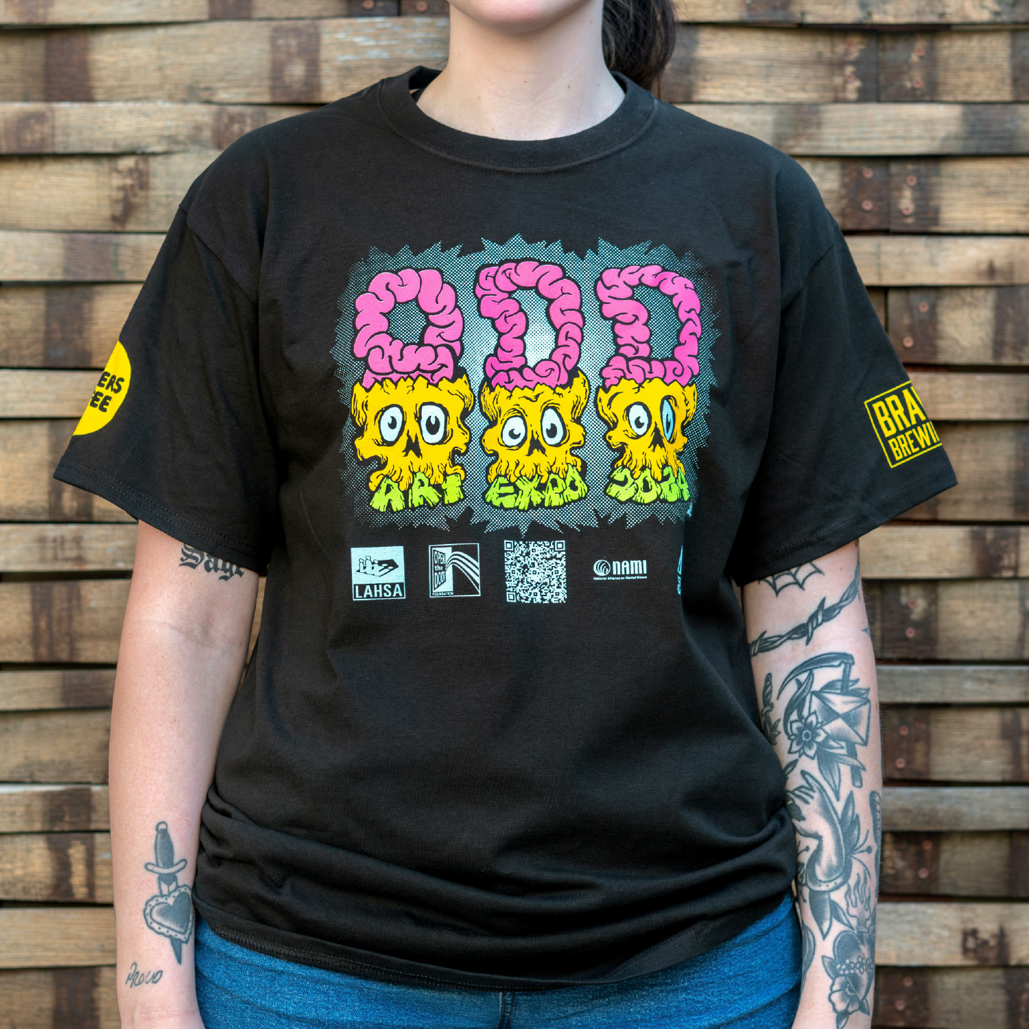 Photo of a person wearing a shirt facing the camera. The shirt is black in color with a colorful graphic print that reads "ODD ART EXPO 2024" across the chest.